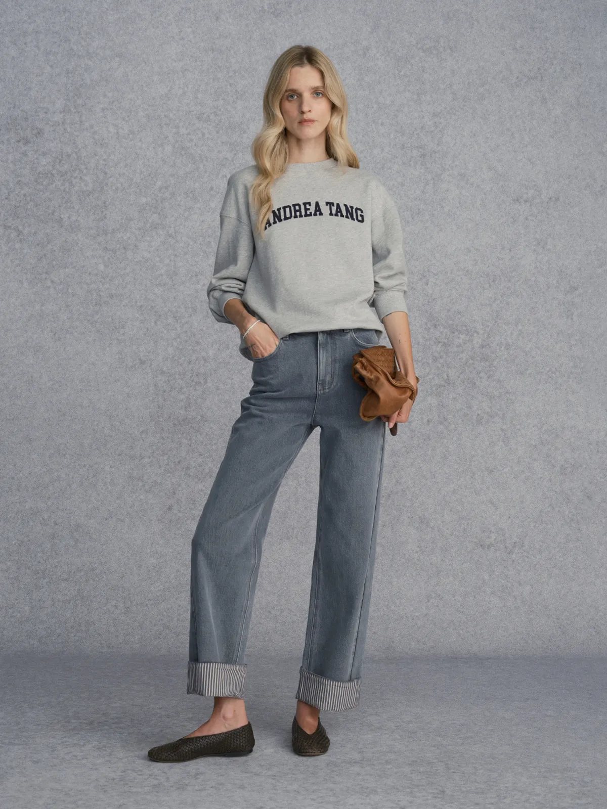 Model wearing Andrea Tang FLIPSIDE Stripe Cuffed Jeans with grey sweatshirt and woven leather flats against textured grey backdrop