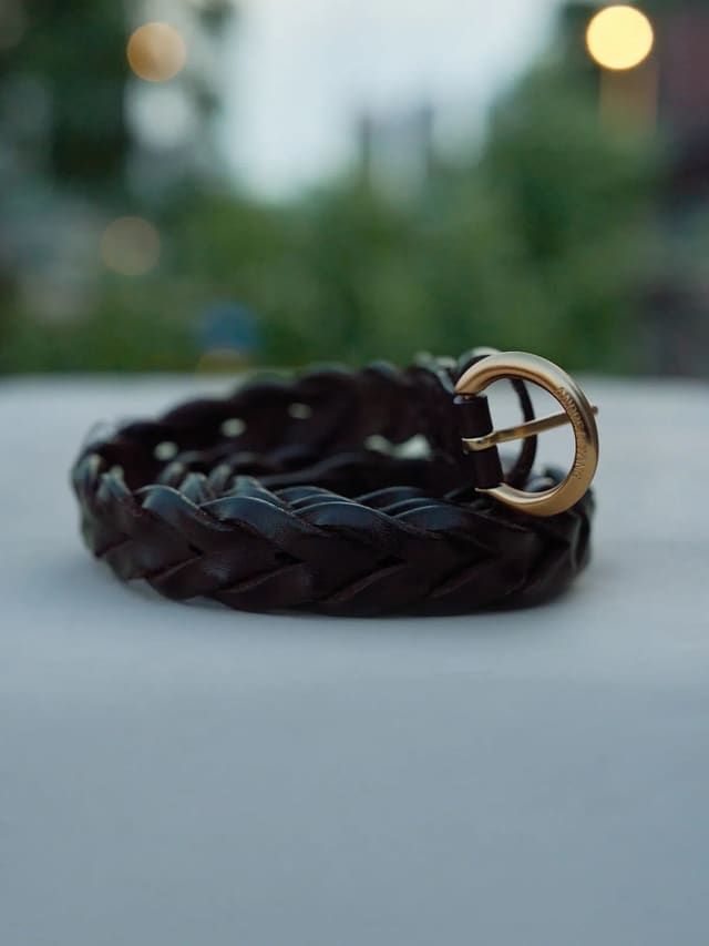 Close-up of Andreatang PLAIT belt buckle with engraved brand name on bokeh background