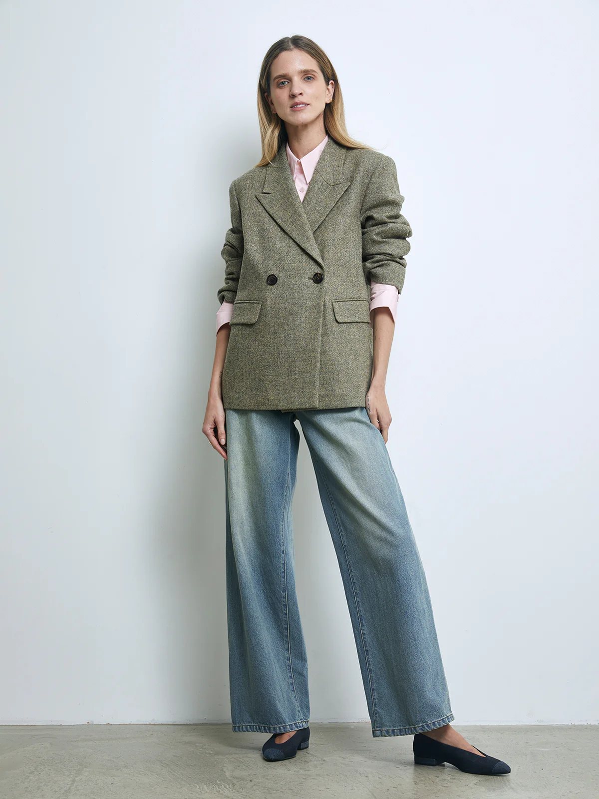 Front view of a model wearing a Sage Green pure wool tweed double-breasted blazer with notched lapels and flap pockets over a dress.