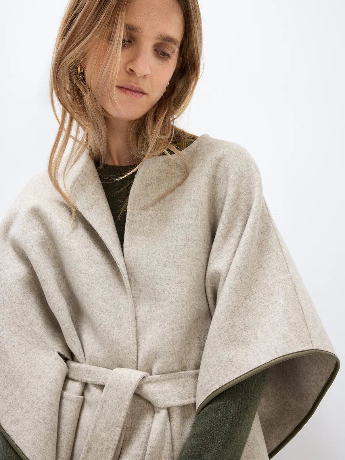 Front view of a model in a Beige cape coat with self-tie belt, open front, and contrasting sleeve lining over a dress.
