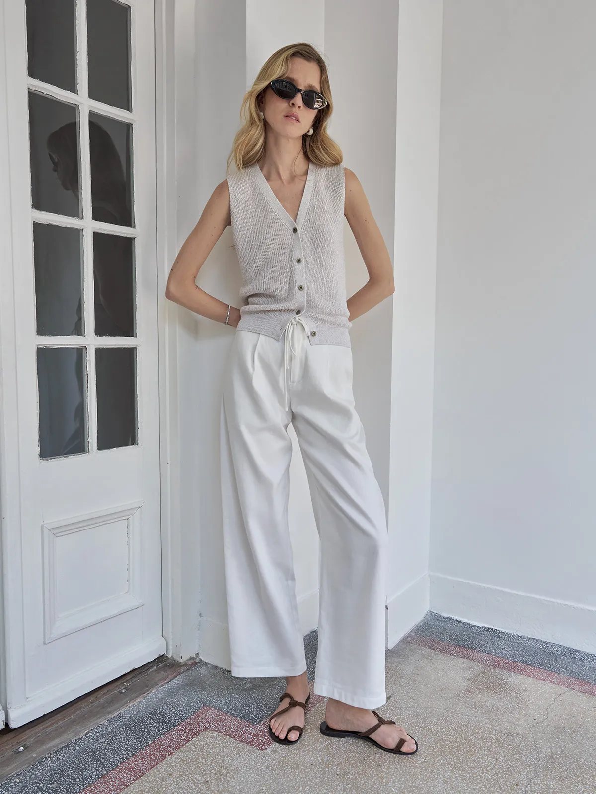 Model in light gray ZOLA vest with white drawstring trousers and tortoiseshell sunglasses