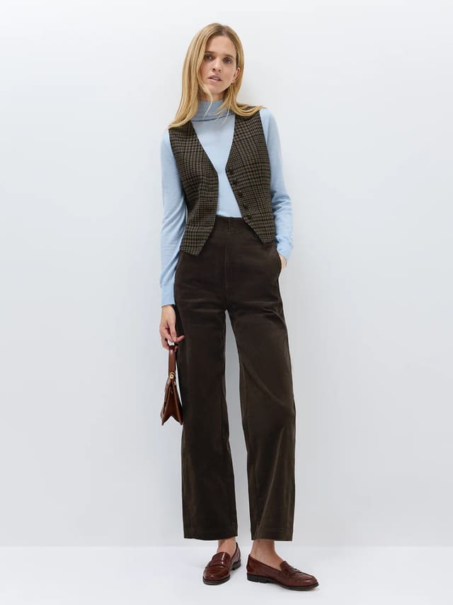 Model wearing andreatang deep-brown wool-blend vintage check vest over light blue turtleneck with dark brown wide-leg cords