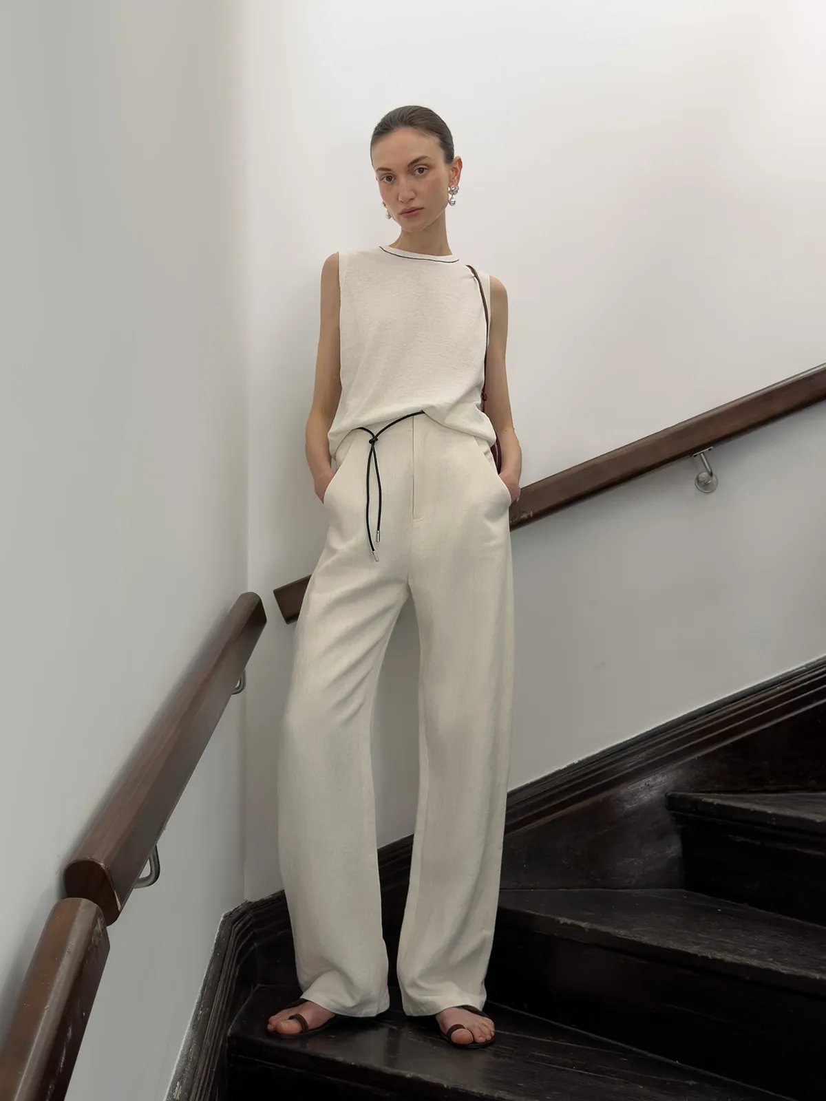 Model on staircase wearing ivory sleeveless knit top with wide-leg trousers and drawstring waist