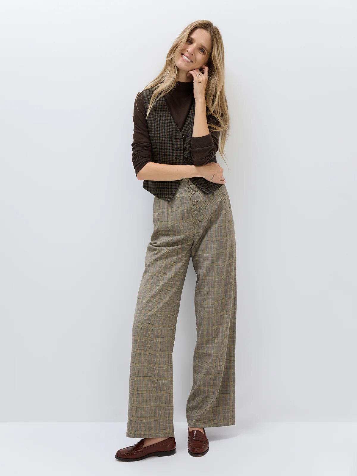 Close-up of high-waisted wide-leg Prince of Wales check trousers showing pleats and vertical four-button detail.