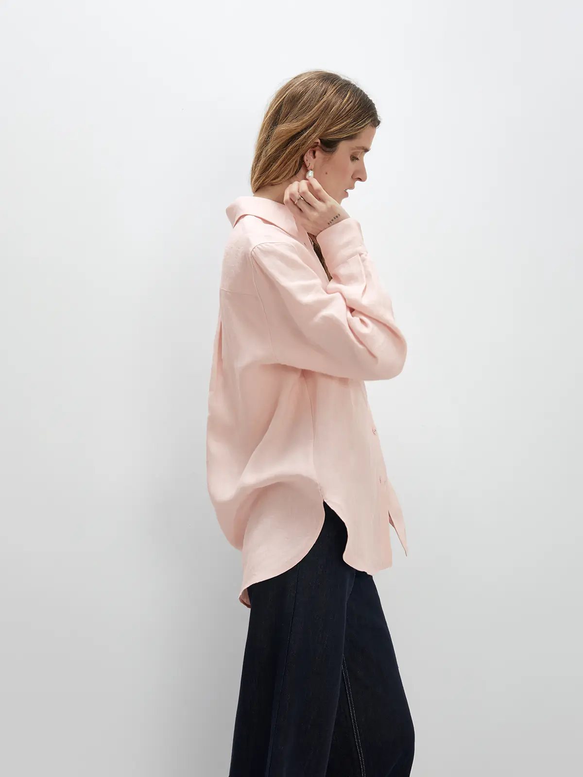 model with arms crossed, wearing a Pink linen shirt with voluminous rolled sleeves and light trousers.