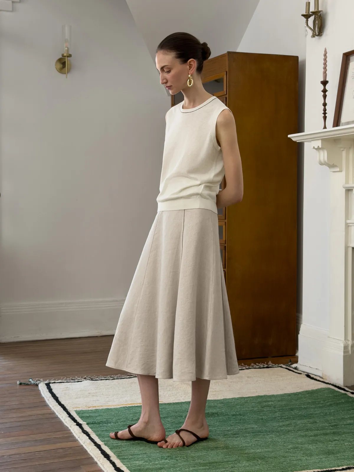 Side profile of model in NATASHA skirt and cream knit, standing near fireplace and cabinet