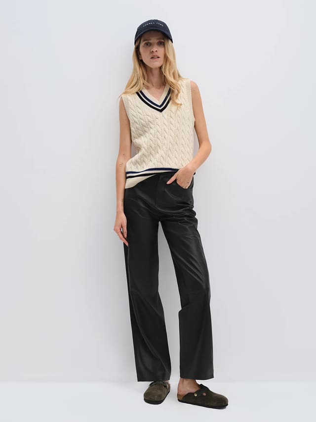 Model wearing andreatang wool-cotton cable-knit cricket vest with contrast stripes, styled with black leather pants and cap