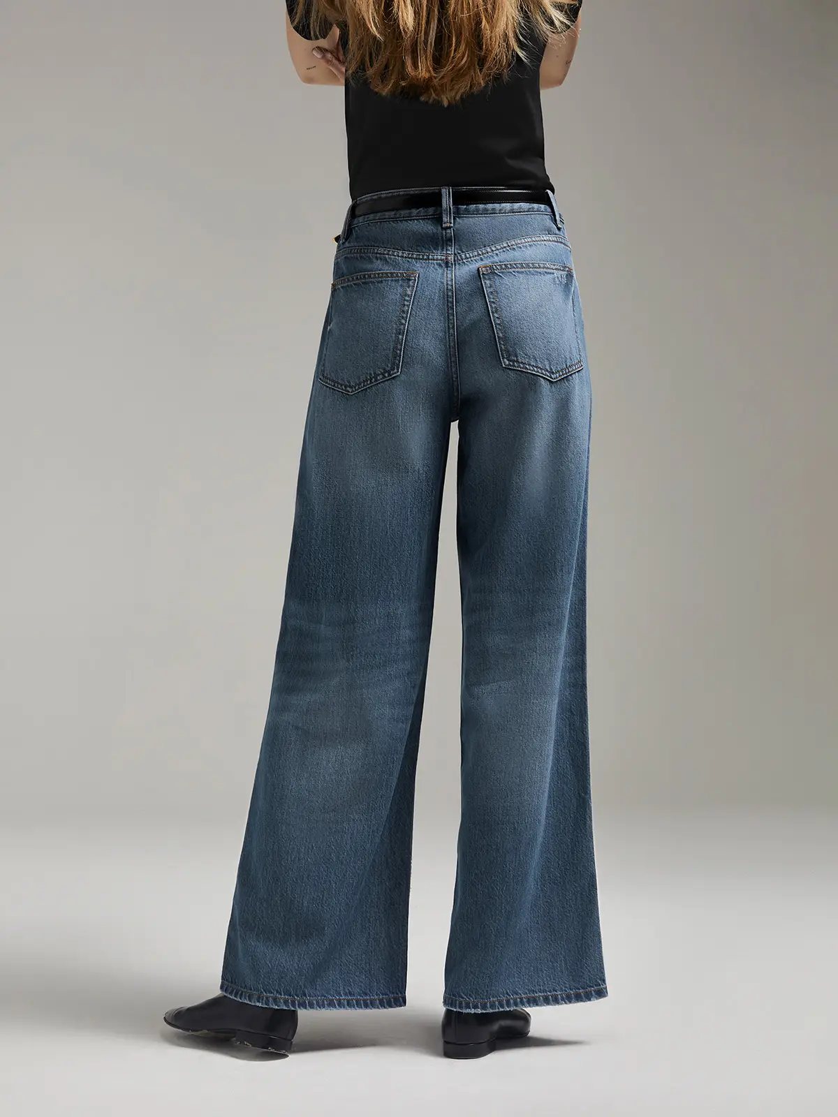 Back view of model wearing Blue mid-low waist wide-leg jeans with top and shoes.