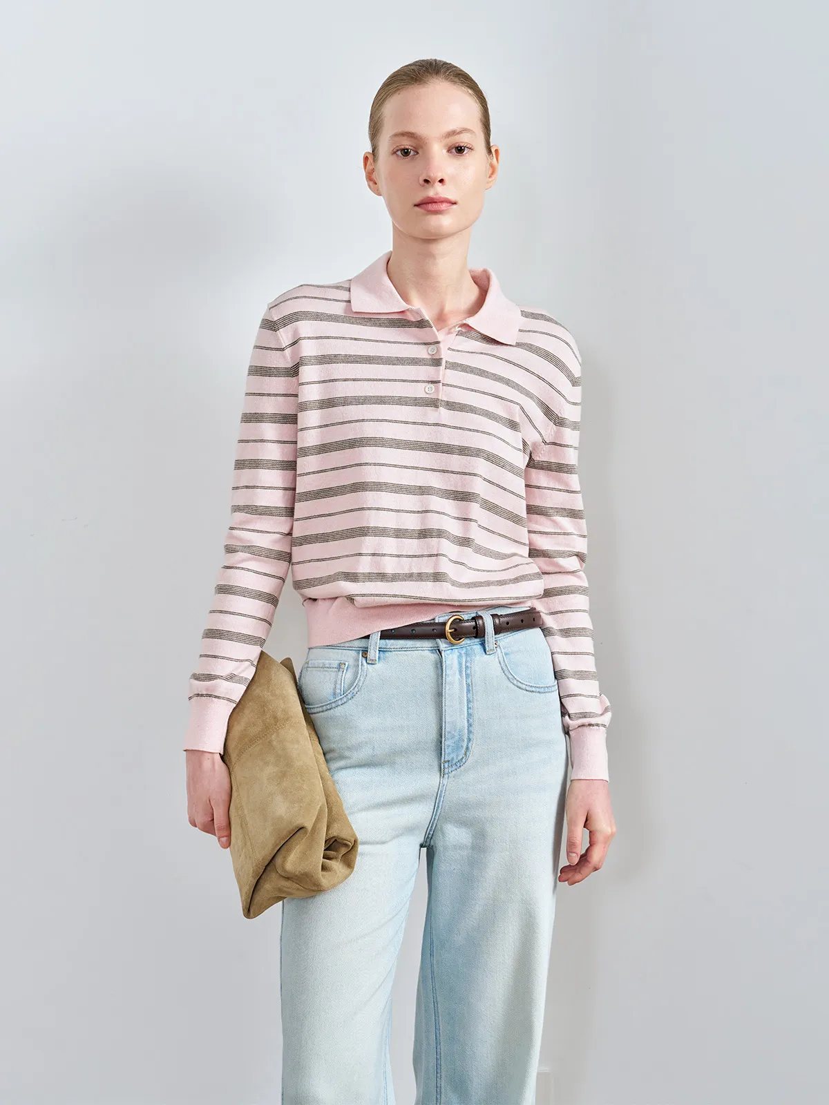 Studio front view of model in HELENA striped polo top, light wash jeans, brown belt, and tan clutch