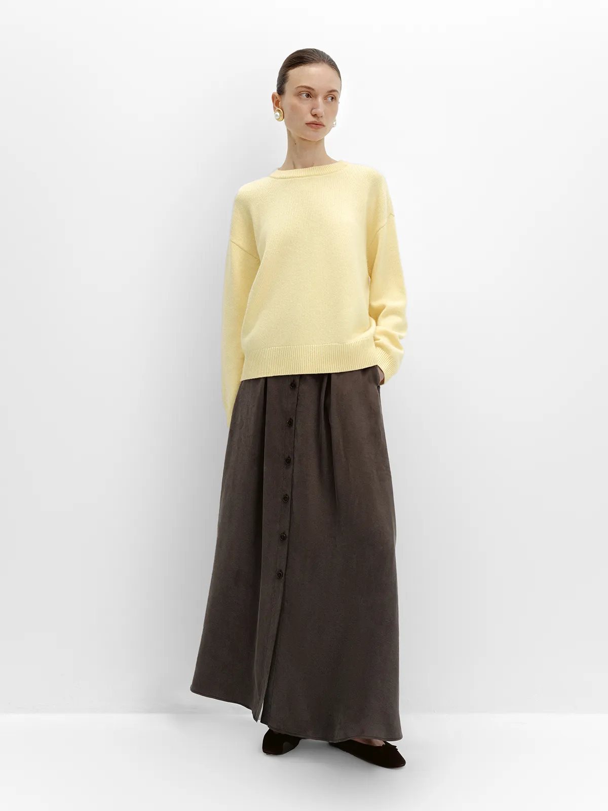 Model in taupe NOBU Maxi Skirt with pale yellow sweater, seated pose emphasizing drape and slit