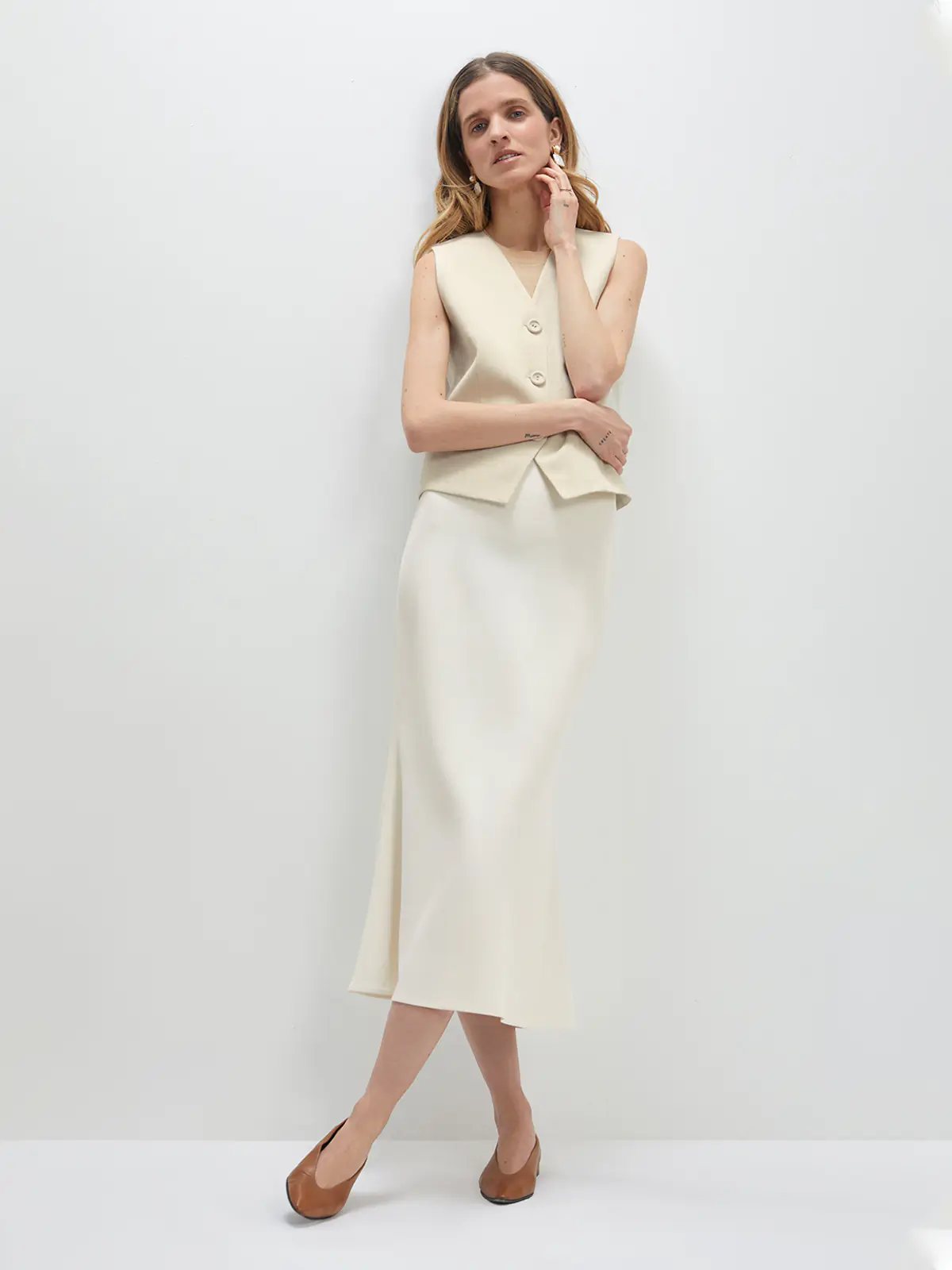 Model wearing an acetate mermaid skirt with a matching sleeveless vest and flats, front view.