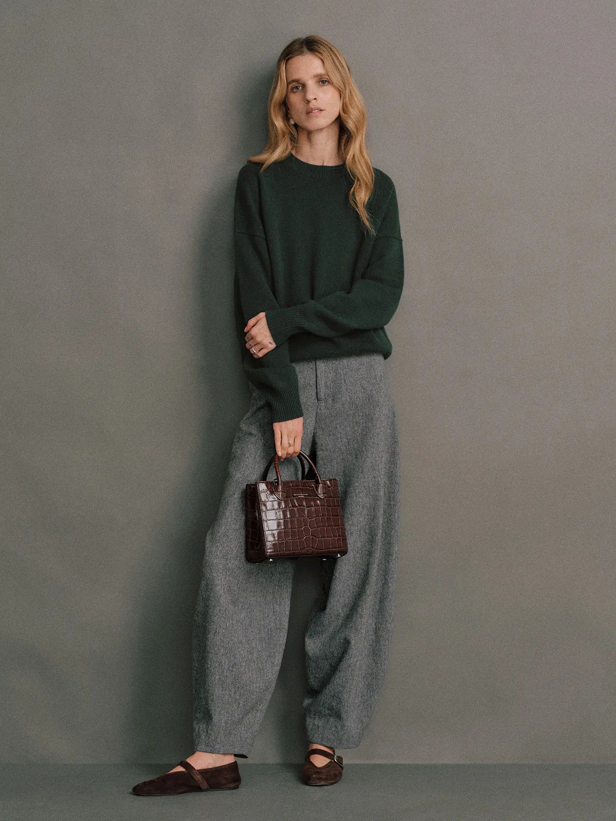 Model in a Black merino wool crewneck jumper, hands in pockets, wearing black leather trousers and hoop earrings.