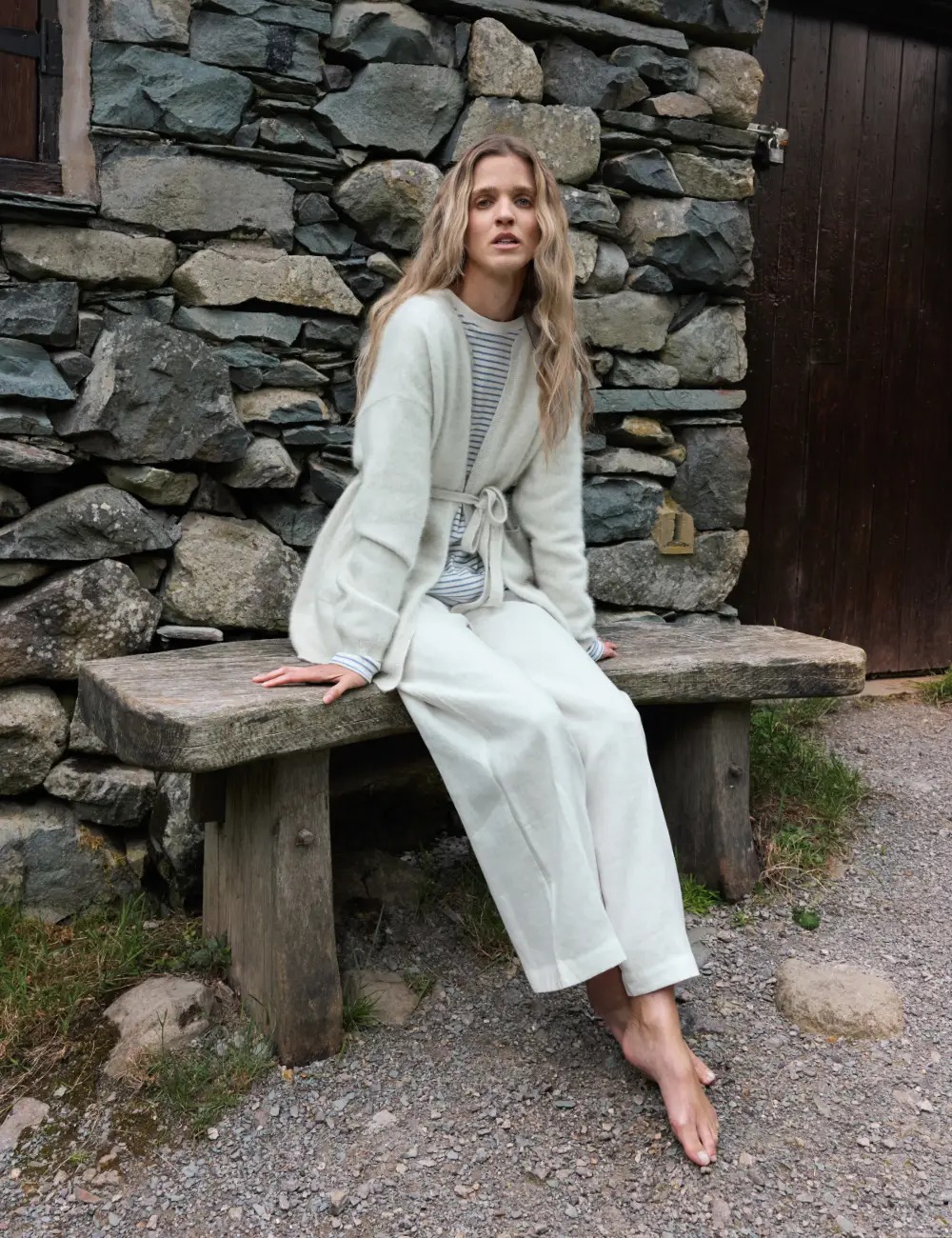 Woman in a pale tailored look seated beside a stone wall