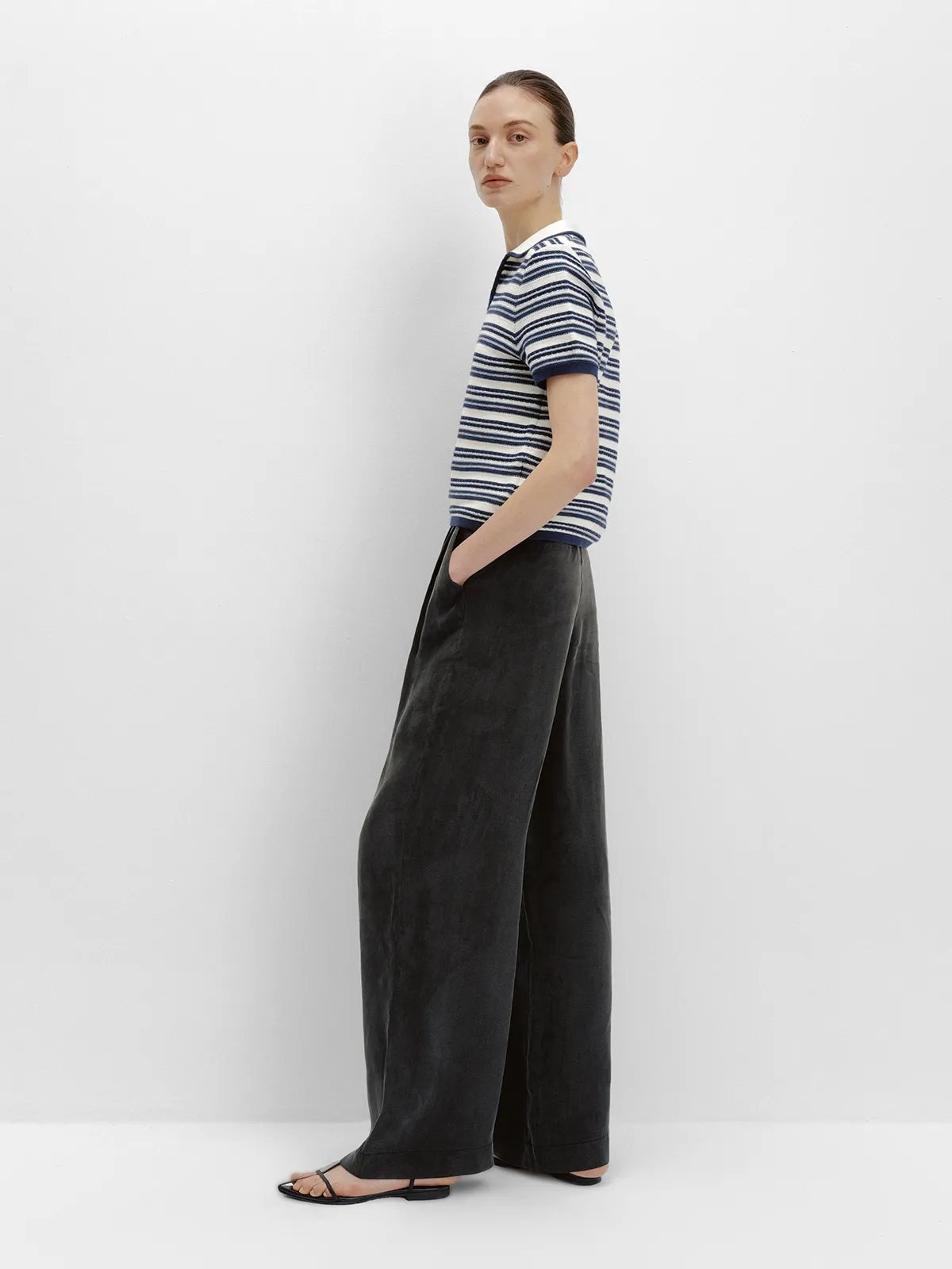Side view of model in black NOBU Trousers with navy-and-white striped knit polo