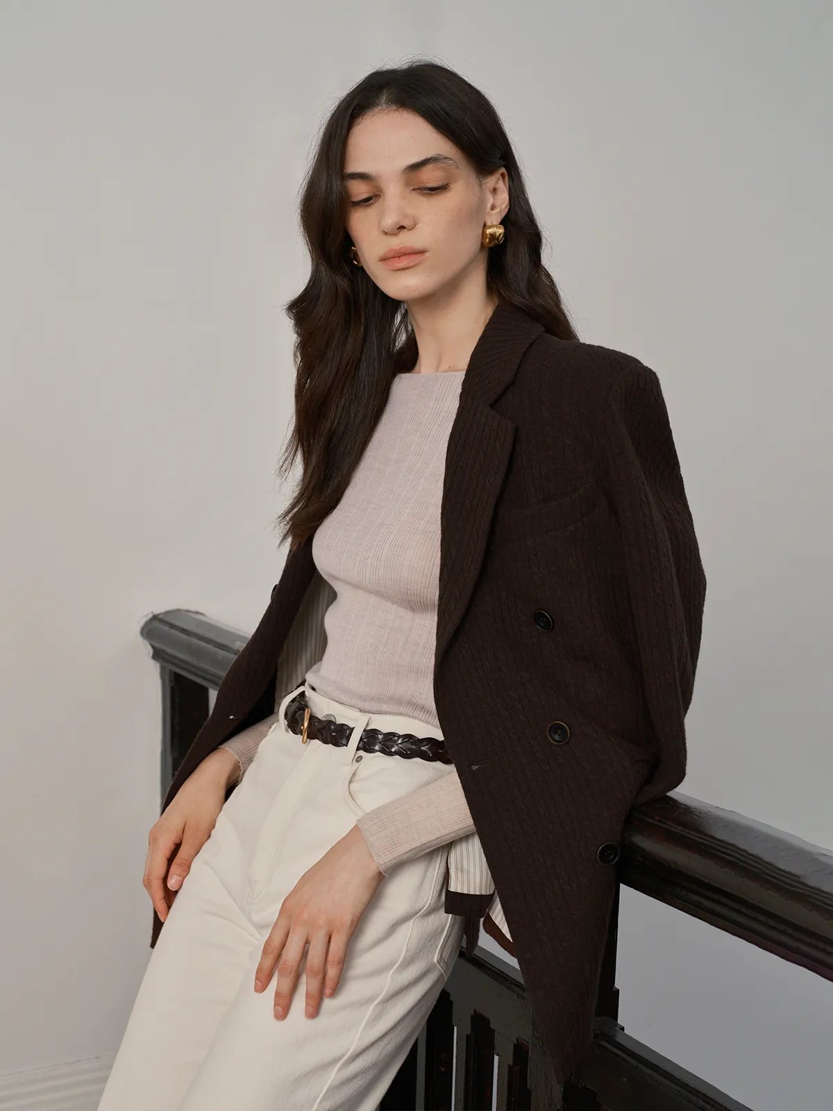 Model leaning on railing in Andreatang THERESA top, brown blazer, and white trousers