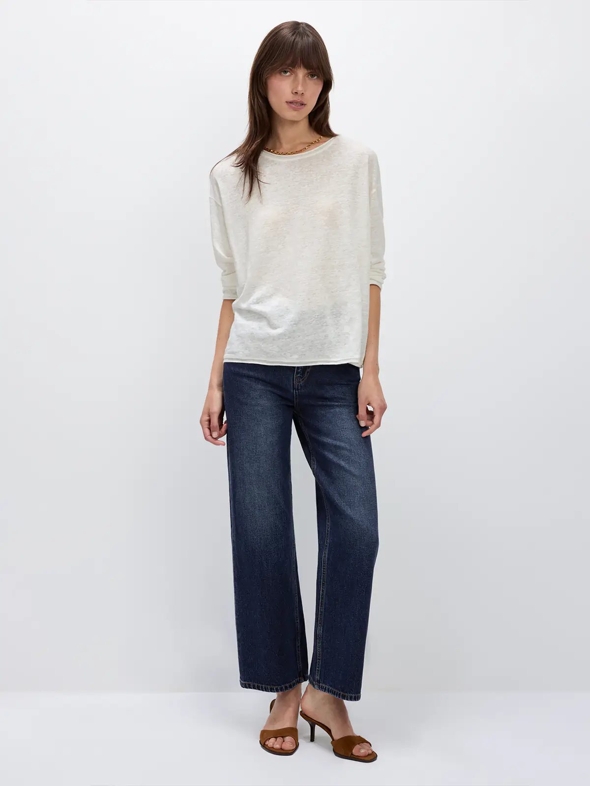 Model wearing a white lightweight long-sleeve linen t-shirt with relaxed fit and rolled sleeves, paired with dark jeans.