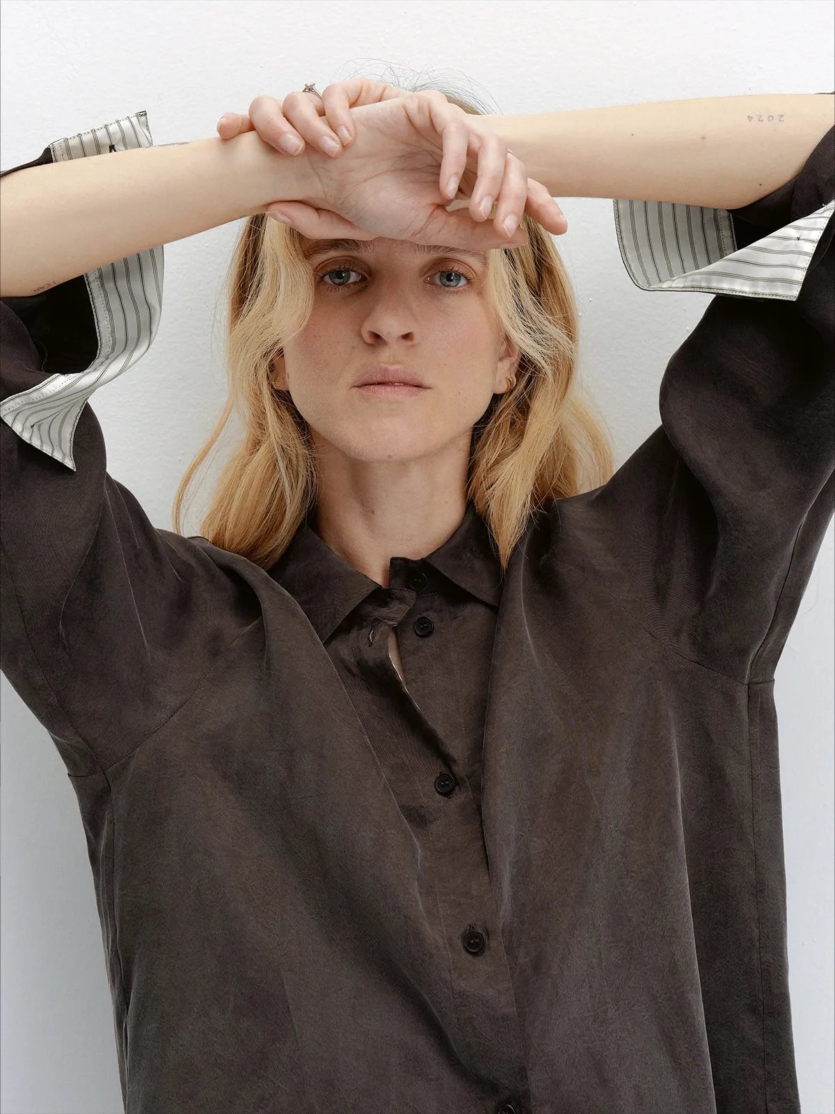 Model wearing andreatang NOBU Shirt in dark taupe, arms raised showing striped contrast cuffs and matte sanded lyocell texture