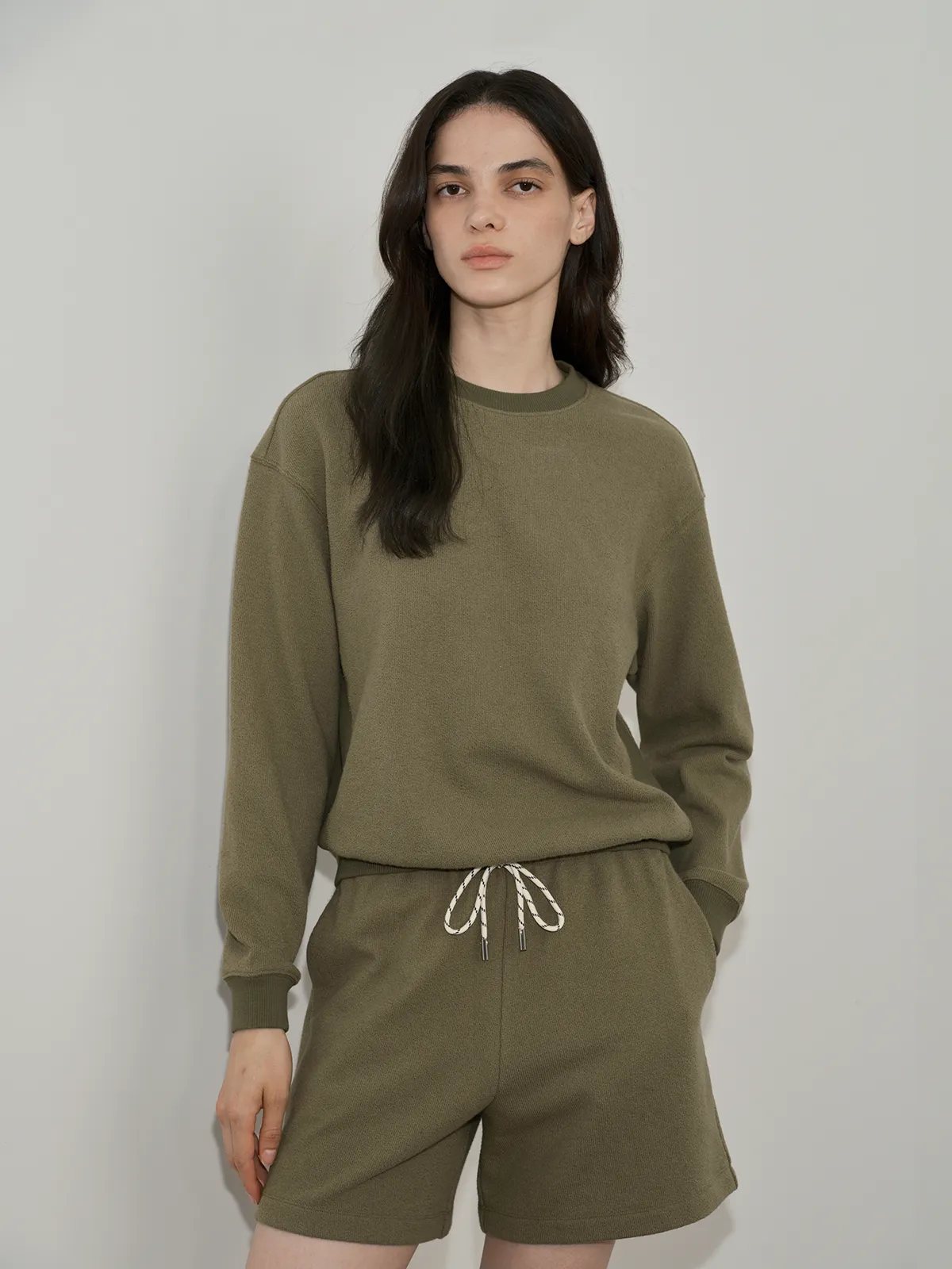 Model in olive green SOREN sweatshirt and shorts front view against neutral background