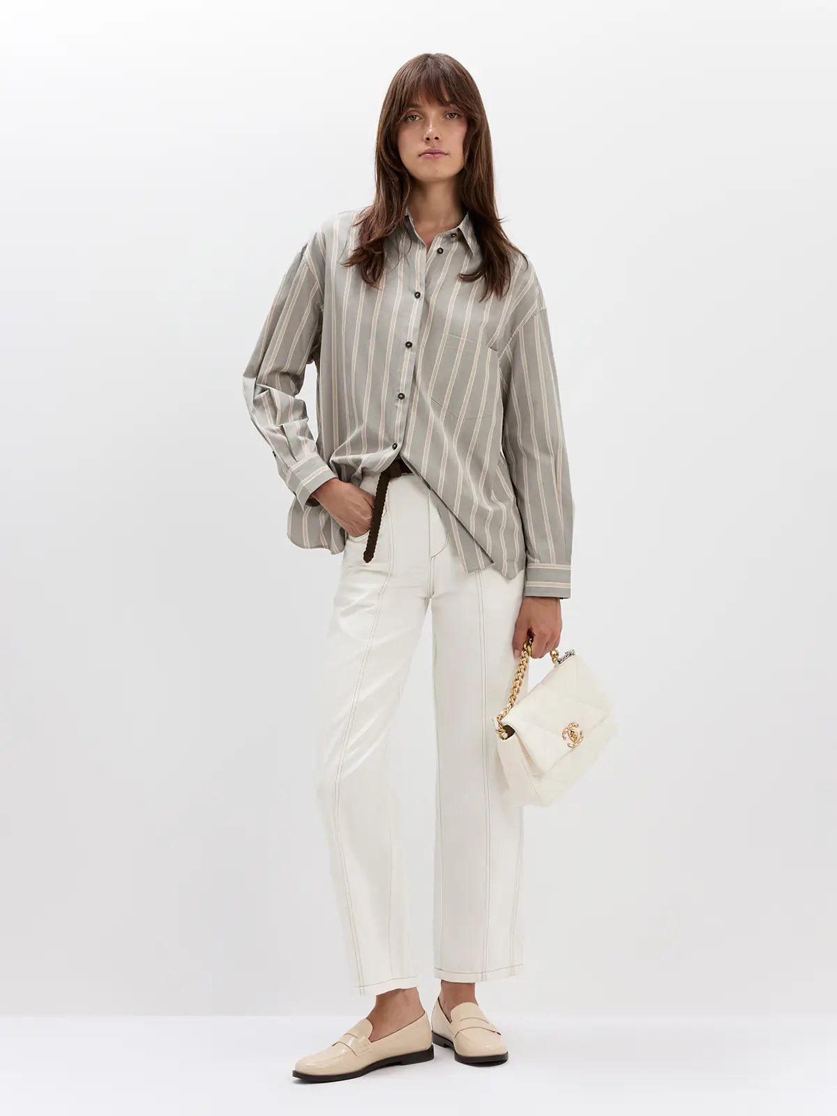 Front view of model wearing white jeans with contrast stitching, a striped sweater, hands in pockets, and loafers.