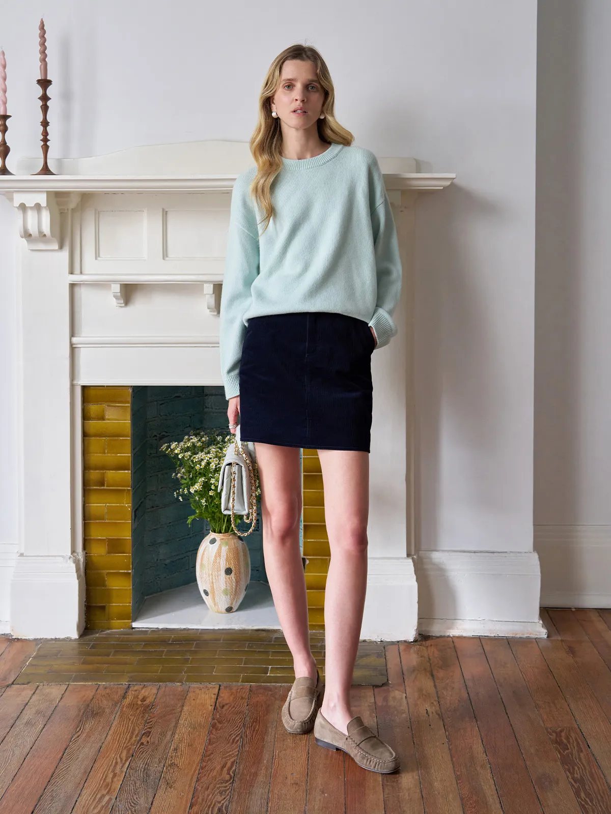 Model wearing navy corduroy DENVER skirt with mint sweater, loafer shoes, and ceramic vase backdrop