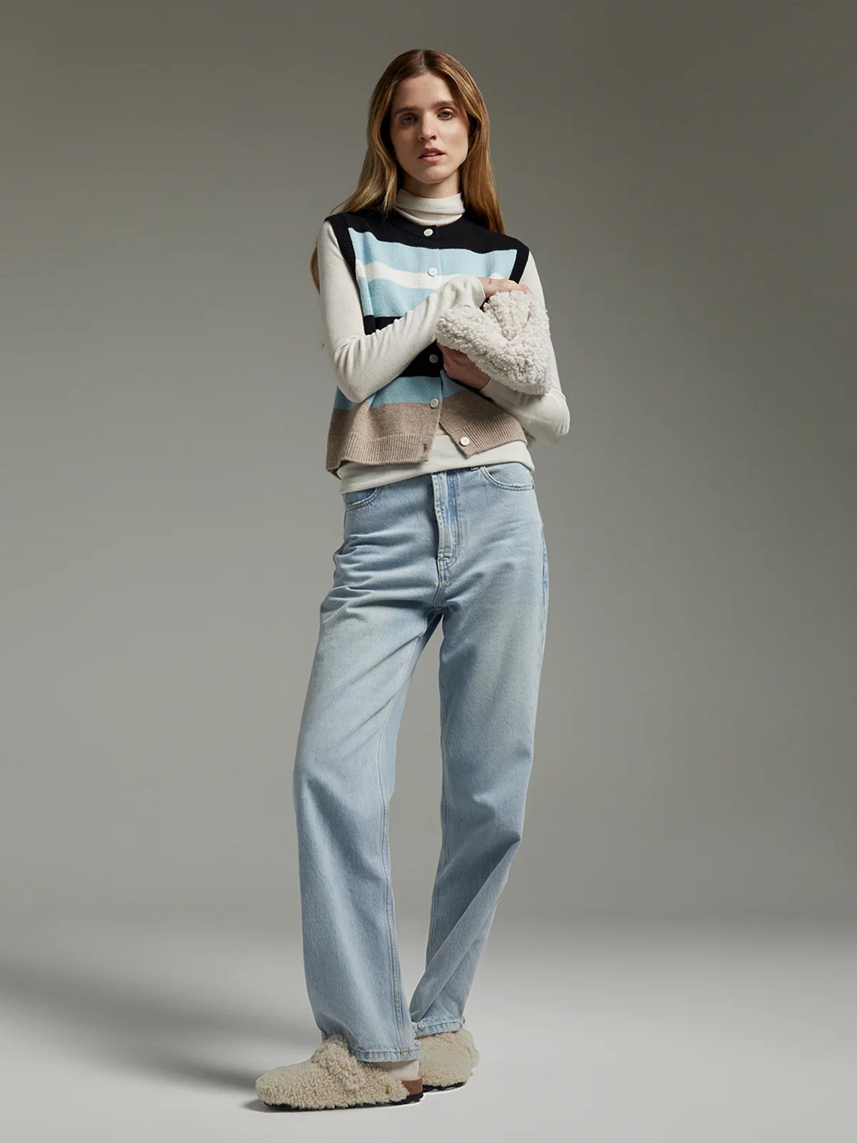 Front view of a model wearing a sleeveless striped patchwork knit vest layered over a collared shirt and jeans.