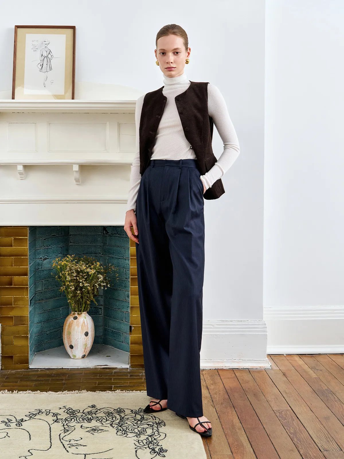 AIDAN vest layered over ivory turtleneck with navy pleated trousers and floral rug