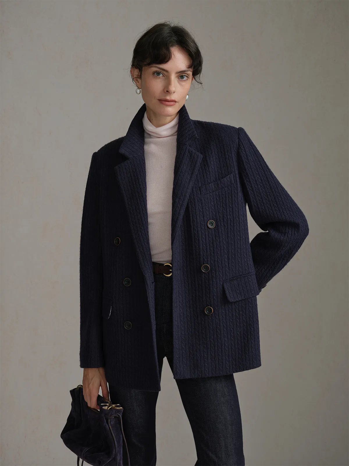 Model in navy HARLOW Cable Knit Blazer with cream turtleneck, belted jeans, and velvet clutch—front pose with hands in pockets