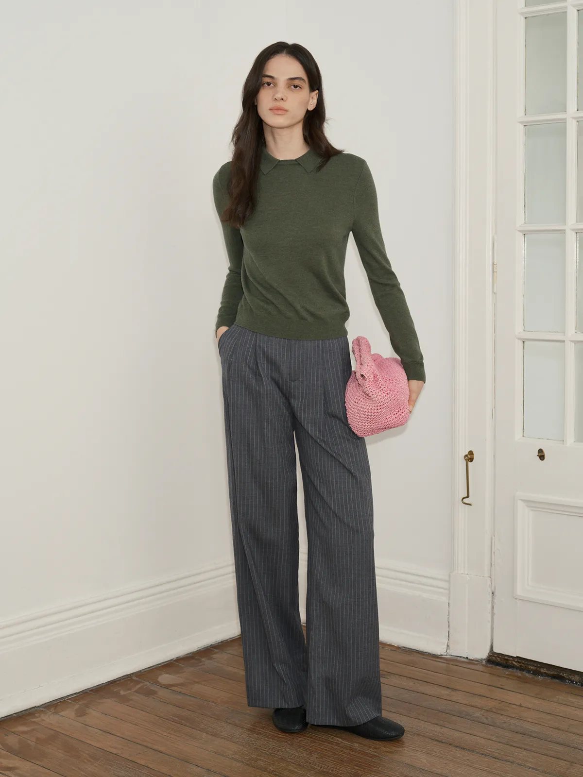 Model wearing olive green LOUANE jumper with grey pinstripe trousers and pink knitted clutch