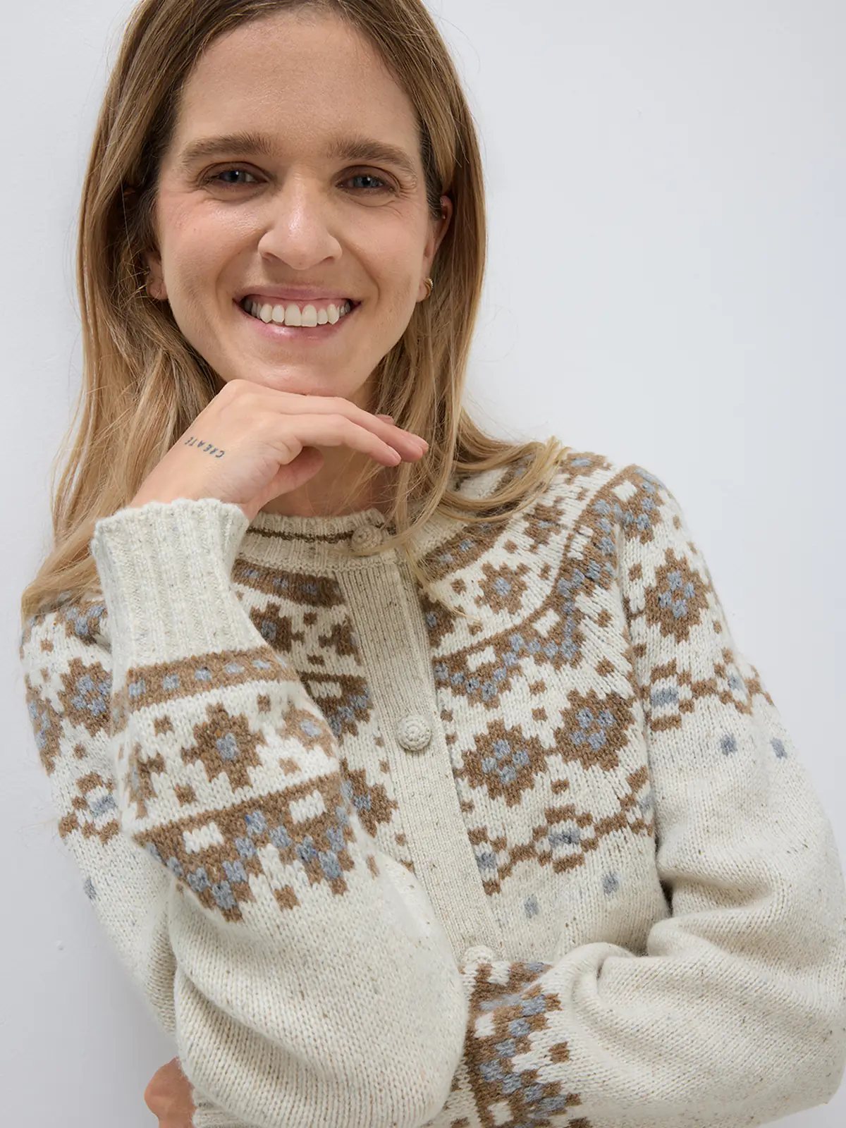 Side view of model in an Oatmeal Fair Isle cardigan with geometric motifs, worn over a top with a skirt and boots.