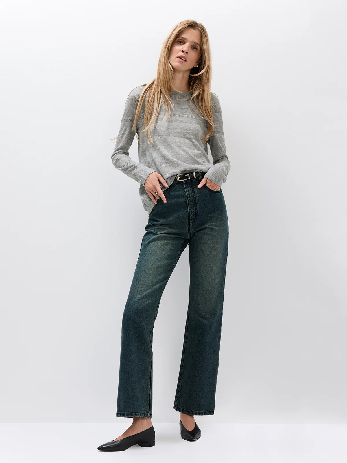 Front view of model wearing Blue mid-rise slim straight jeans with a long-sleeve top and holding a woven bag.