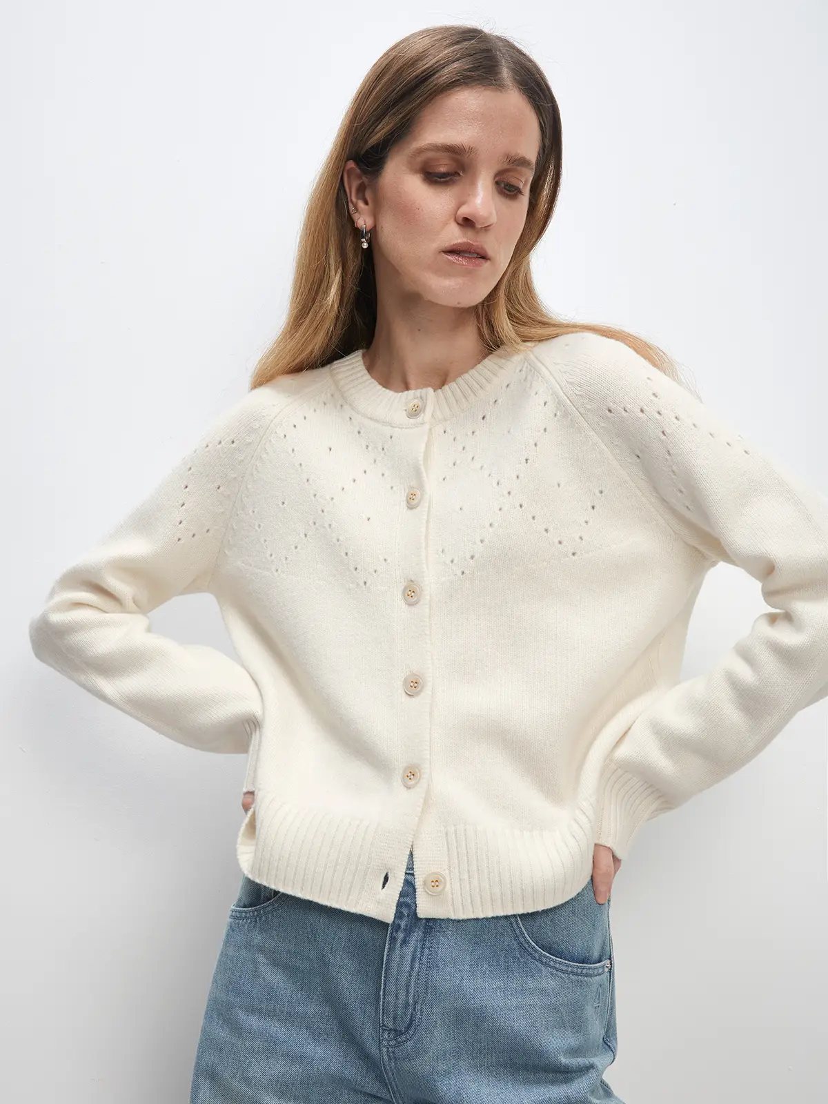 Close front view of white Fair Isle hollowed knitted cardigan showing button placket, ribbed hem, and openwork diamond pattern across chest.
