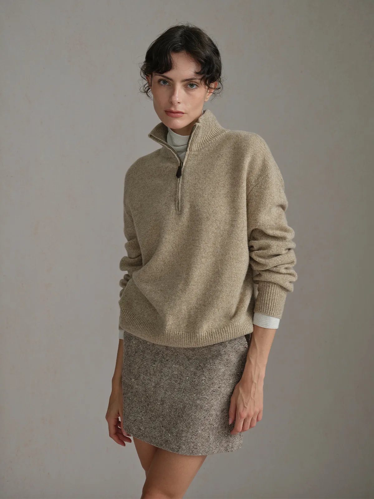 Model in KATIE skirt and beige half-zip sweater, looking directly at camera, arms relaxed, neutral backdrop