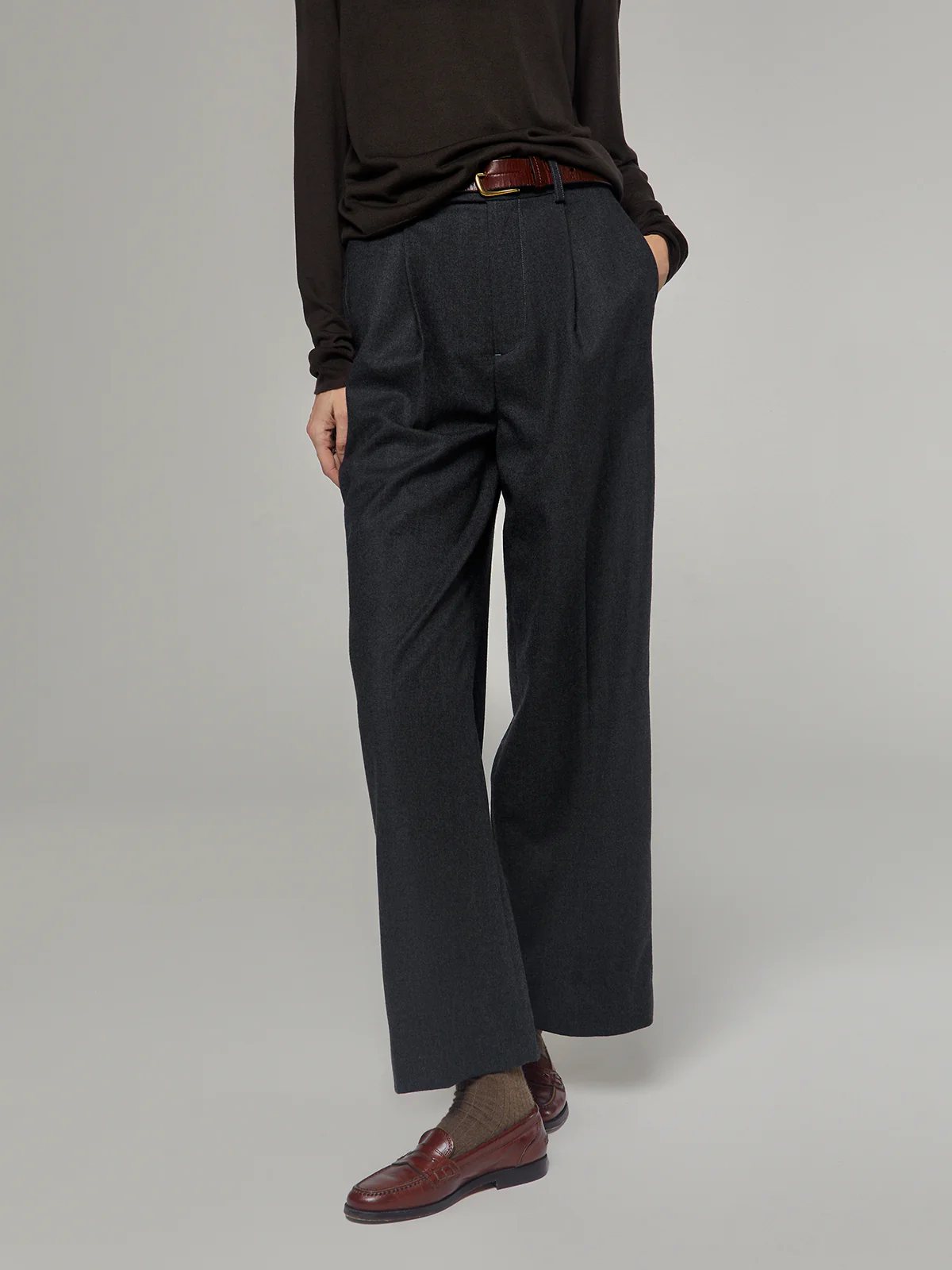 Front view of model wearing Gray fine wool wide-leg trousers with pleated front, tucked-in dark top, and loafers.