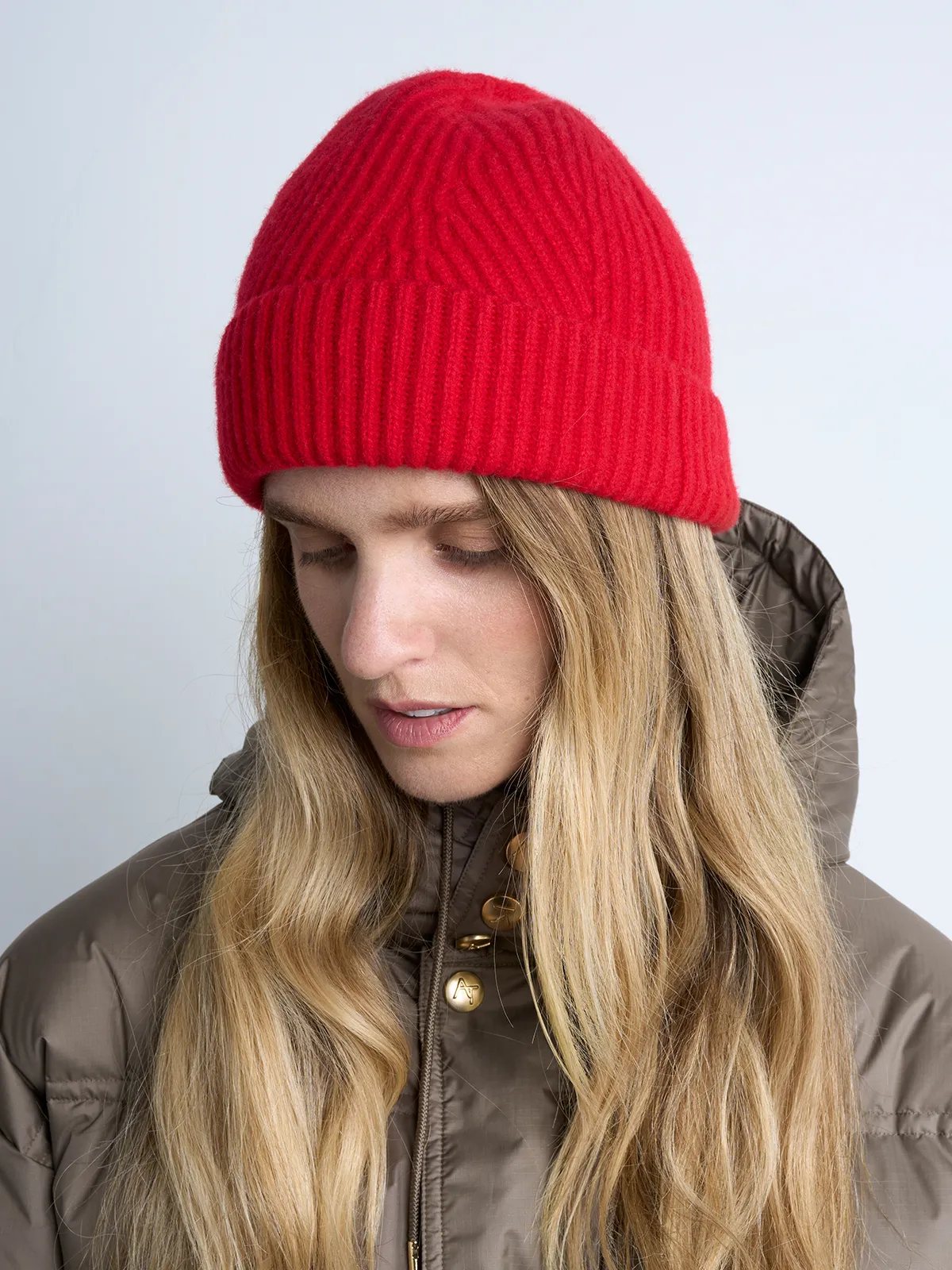 Model looking down while wearing a red ribbed knit beanie and a puffer jacket.