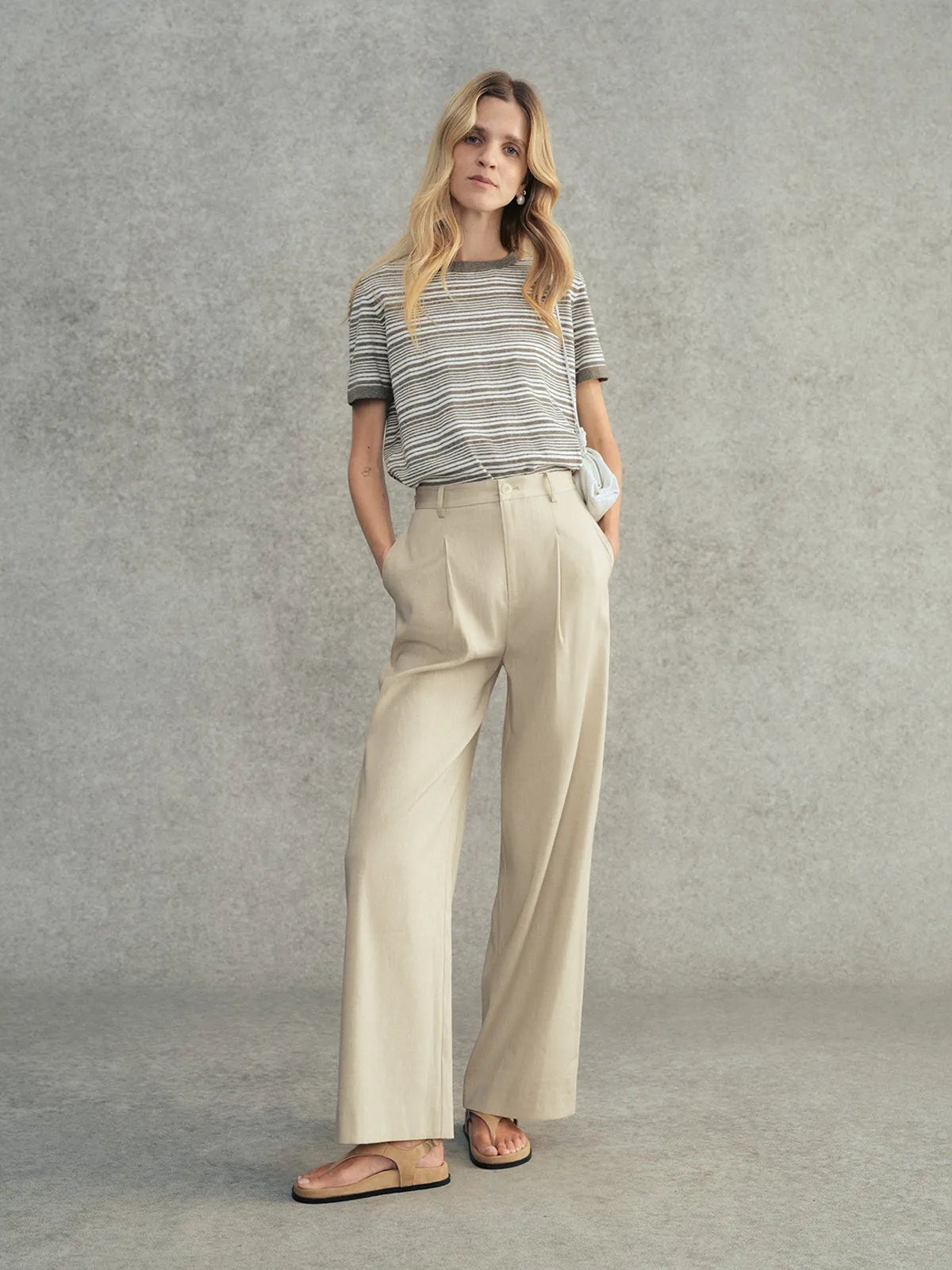 Model wearing charcoal striped JUSTINE t-shirt with beige pleated wide-leg trousers and leather sandals