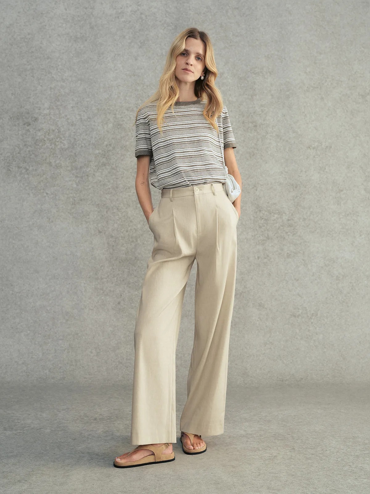 Model wearing charcoal striped JUSTINE t-shirt with beige pleated wide-leg trousers and leather sandals