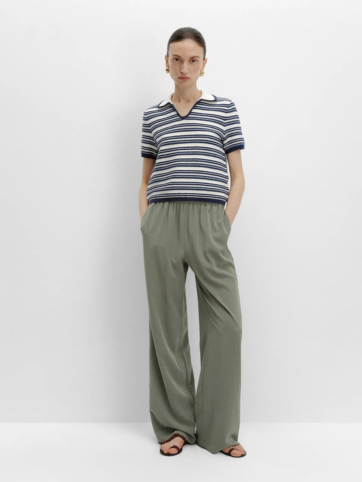 Model in PATRICIA trousers with navy-and-cream striped knit polo, hands in pockets