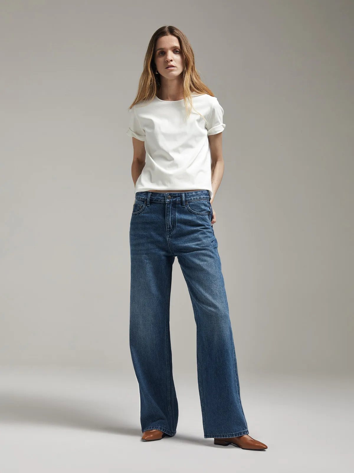 Model in ivory SOSA t-shirt with rolled sleeves, dark wash wide-leg jeans, and brown leather shoes