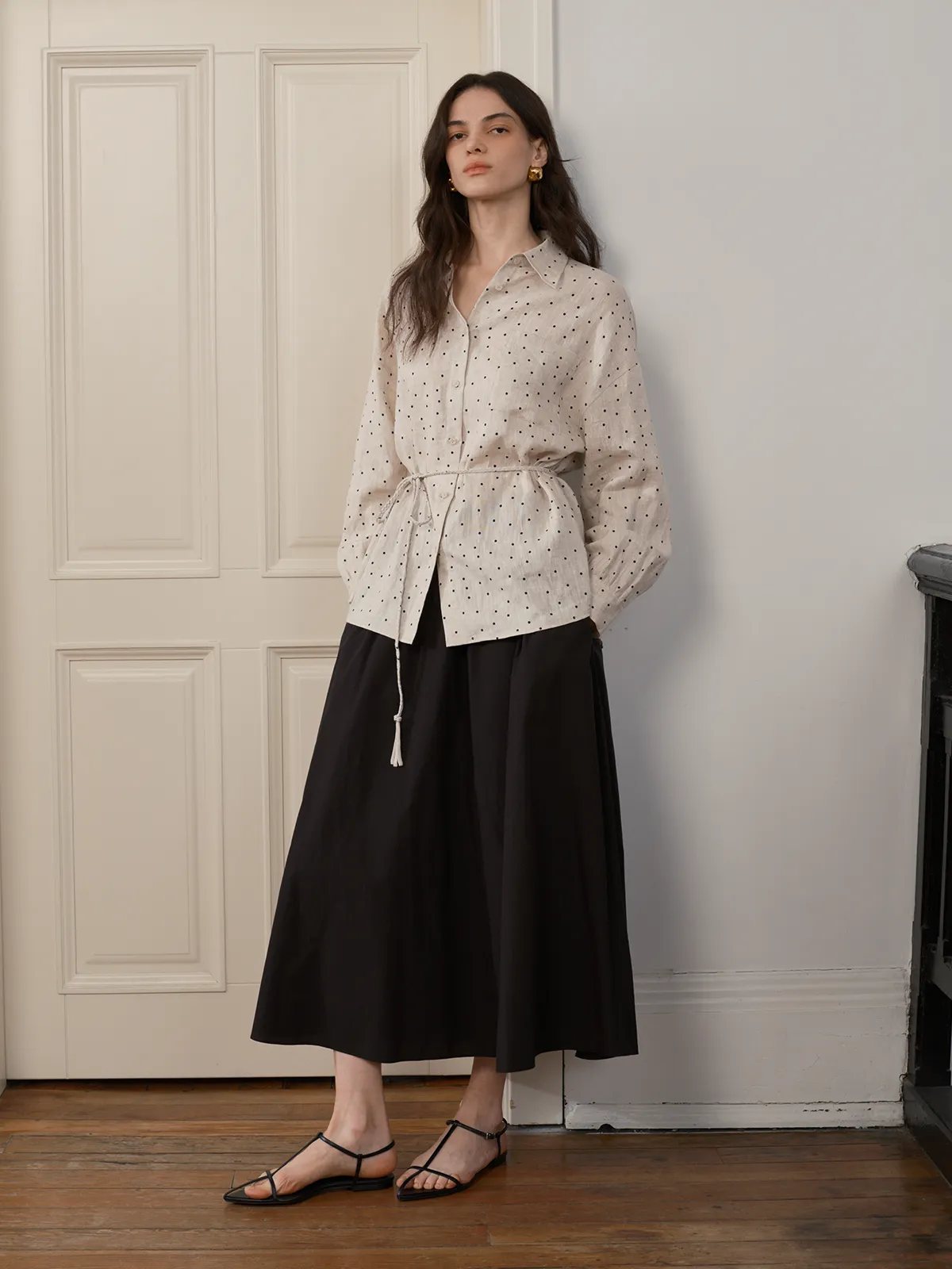 Model wearing ODELIA polka dot linen shirt with tie waist, paired with black A-line midi skirt and minimalist sandals