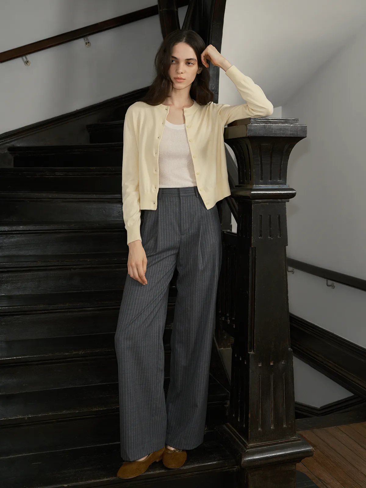 Model wearing BINX cardigan layered over white ribbed tank, leaning on dark wooden staircase