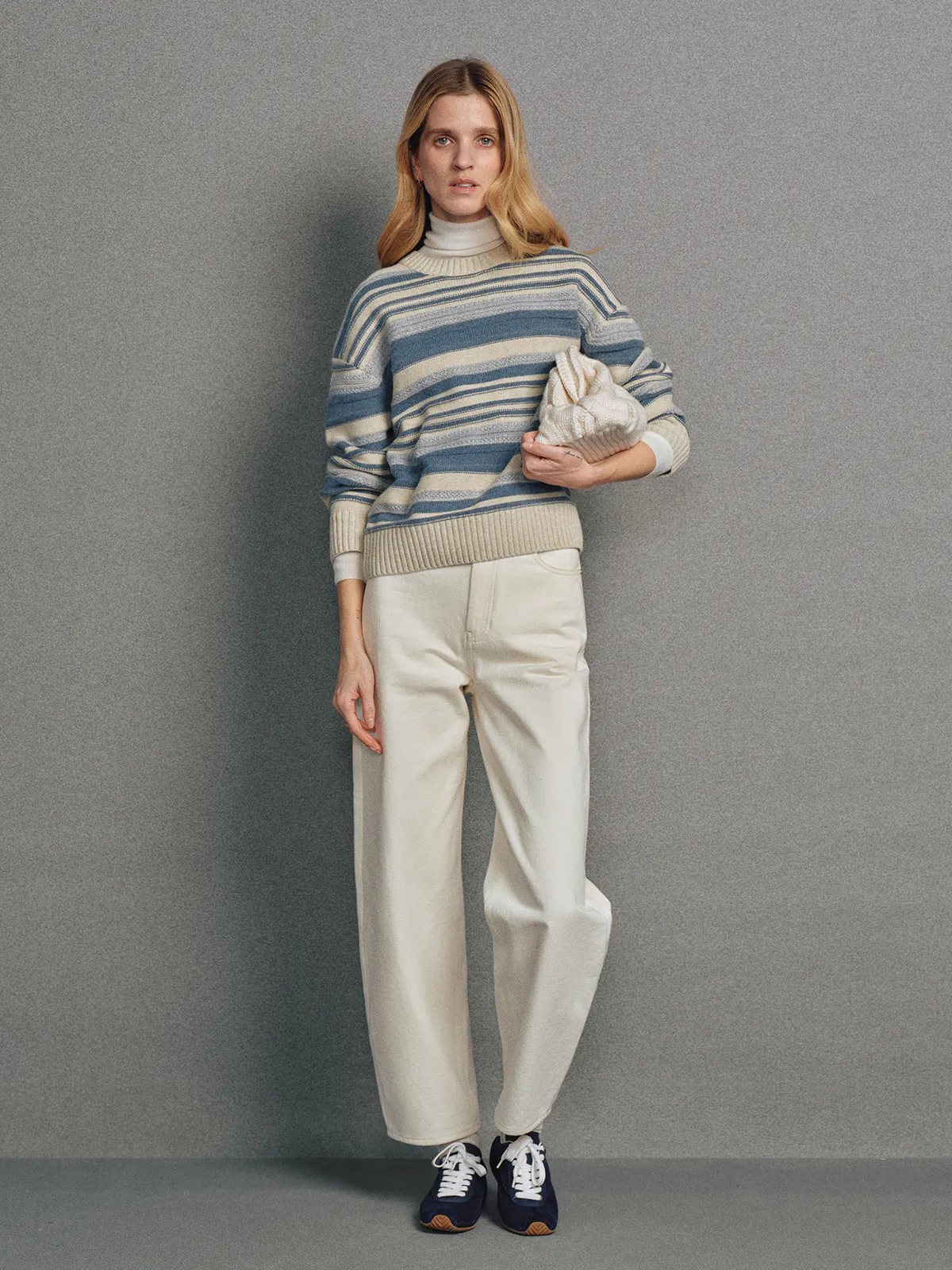 Model wearing a blue irregular multicolour stripe wool cotton jumper with ribbed cuffs and hem.