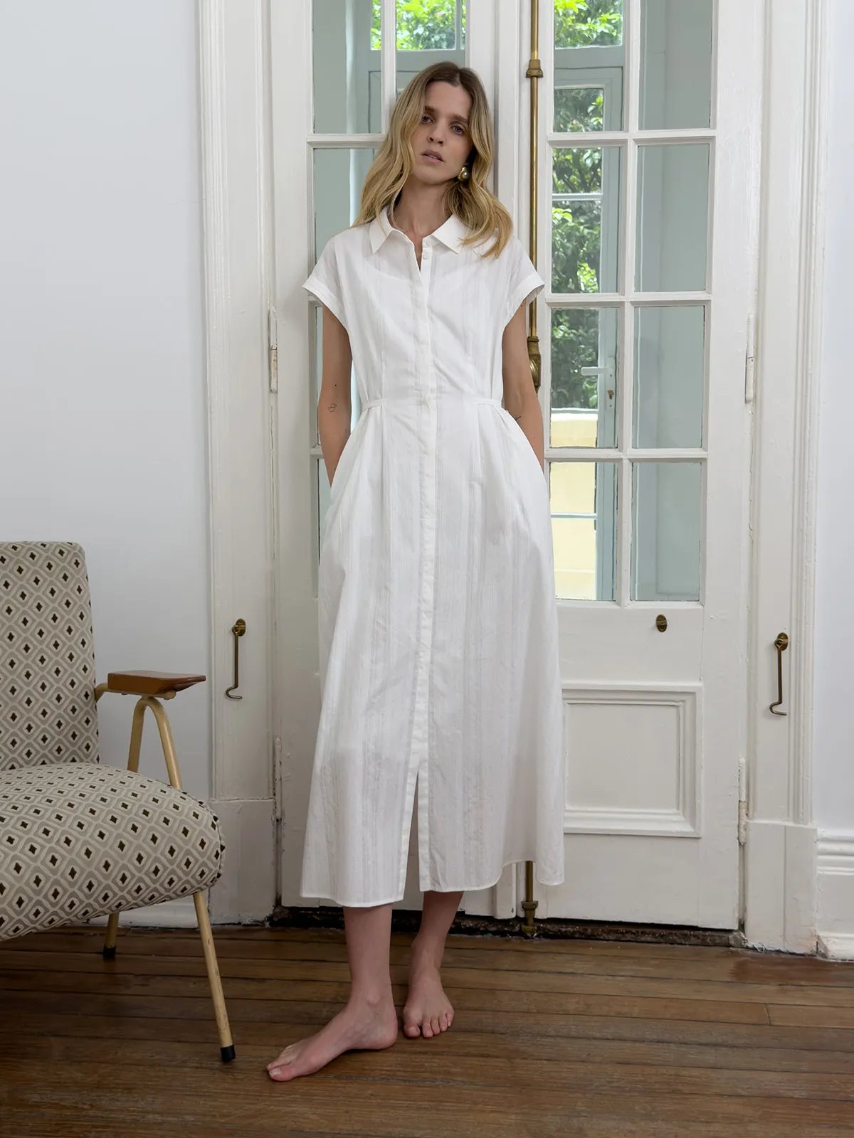 Woman wearing white cotton jacquard shirt dress barefoot in front of French doors