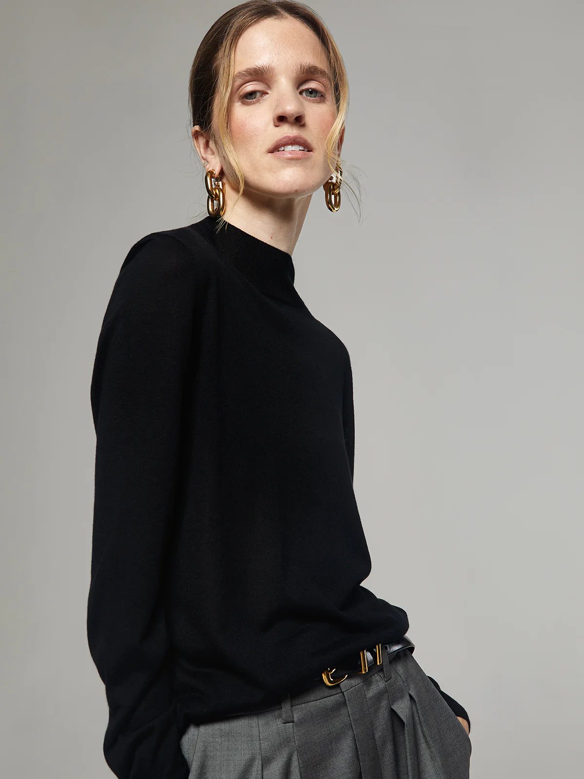 Side view of a model in a black silk lyocell mock-neck top with long sleeves, styled with trousers and earrings.