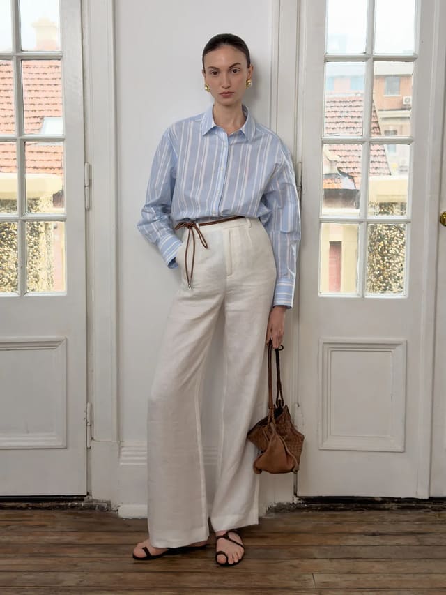 Andrea Tang CLORIS linen straight leg trousers in ivory worn with striped shirt and leather belt, standing by French doors — quiet luxury minimalist styling