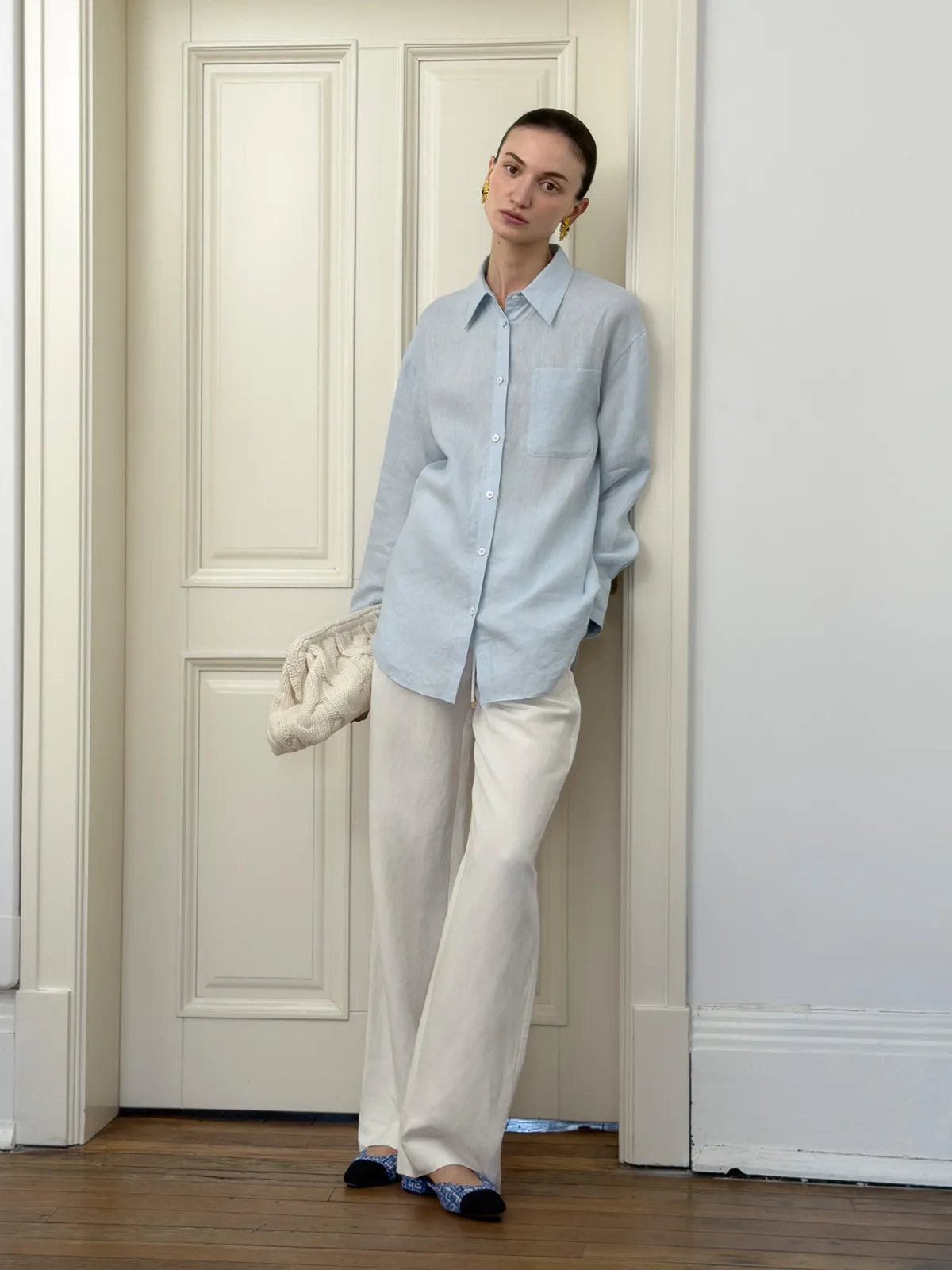 Model wearing light blue linen shirt with white wide-leg trousers and knit clutch