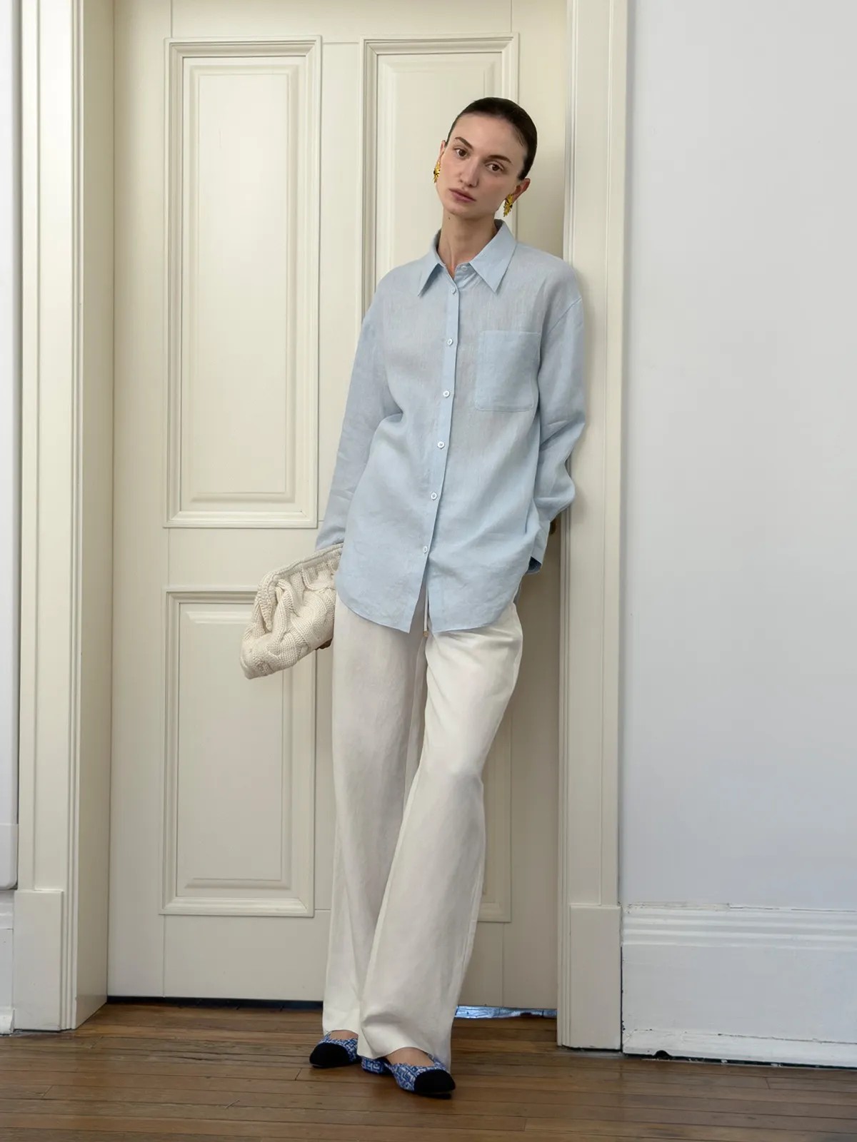 Model wearing light blue linen shirt with white wide-leg trousers and knit clutch