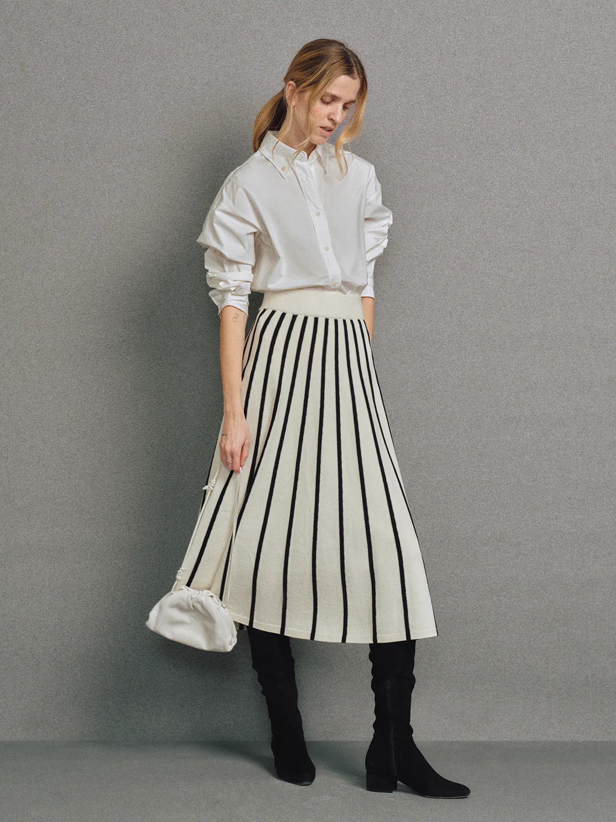 Profile view of a model wearing a Black/White vertical stripe A-line knit skirt with white waistband, white shirt, and black boots.