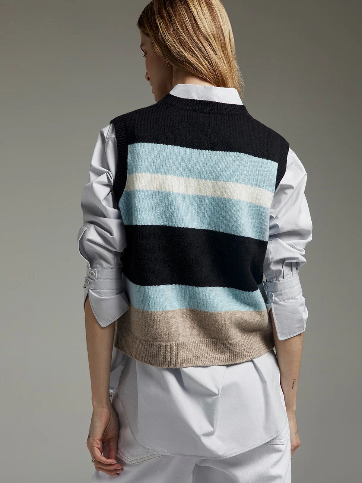 Back view of a model wearing a blue striped patchwork knit vest with, and light blue bands over a shirt.