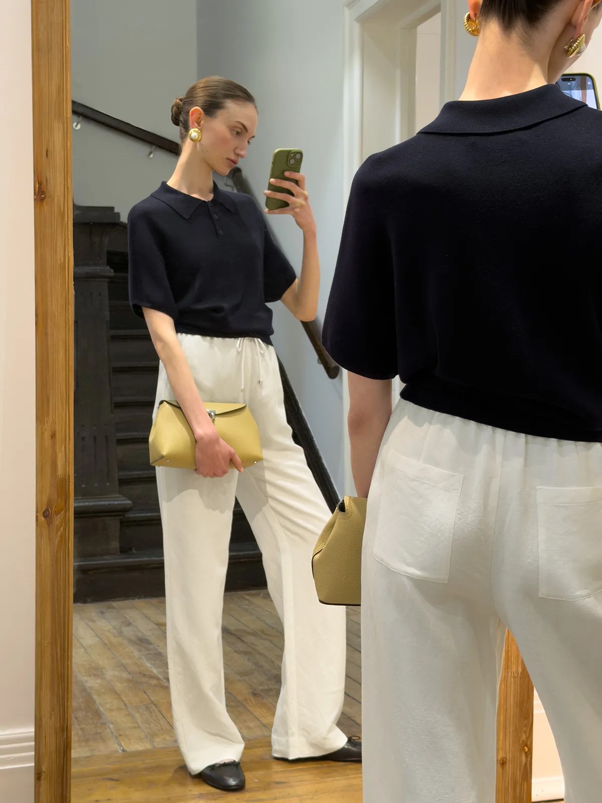 Mirror selfie of model wearing navy NADINE knit polo, white drawstring trousers, and mustard leather bag
