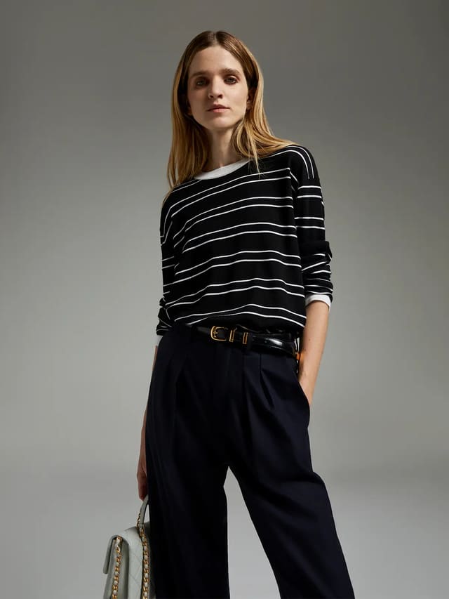 Model wearing a black knit top with horizontal stripes, loose fit, and ribbed cuffs.